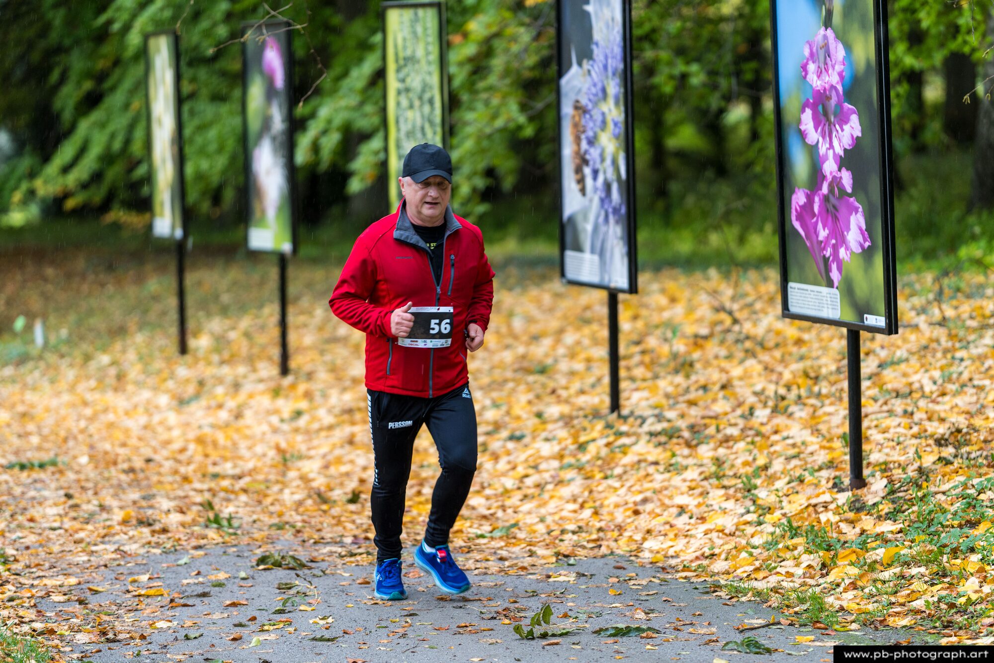 Biegacz w czerwonej kurtce na trasie wśród tablic z fotografiami kwiatów