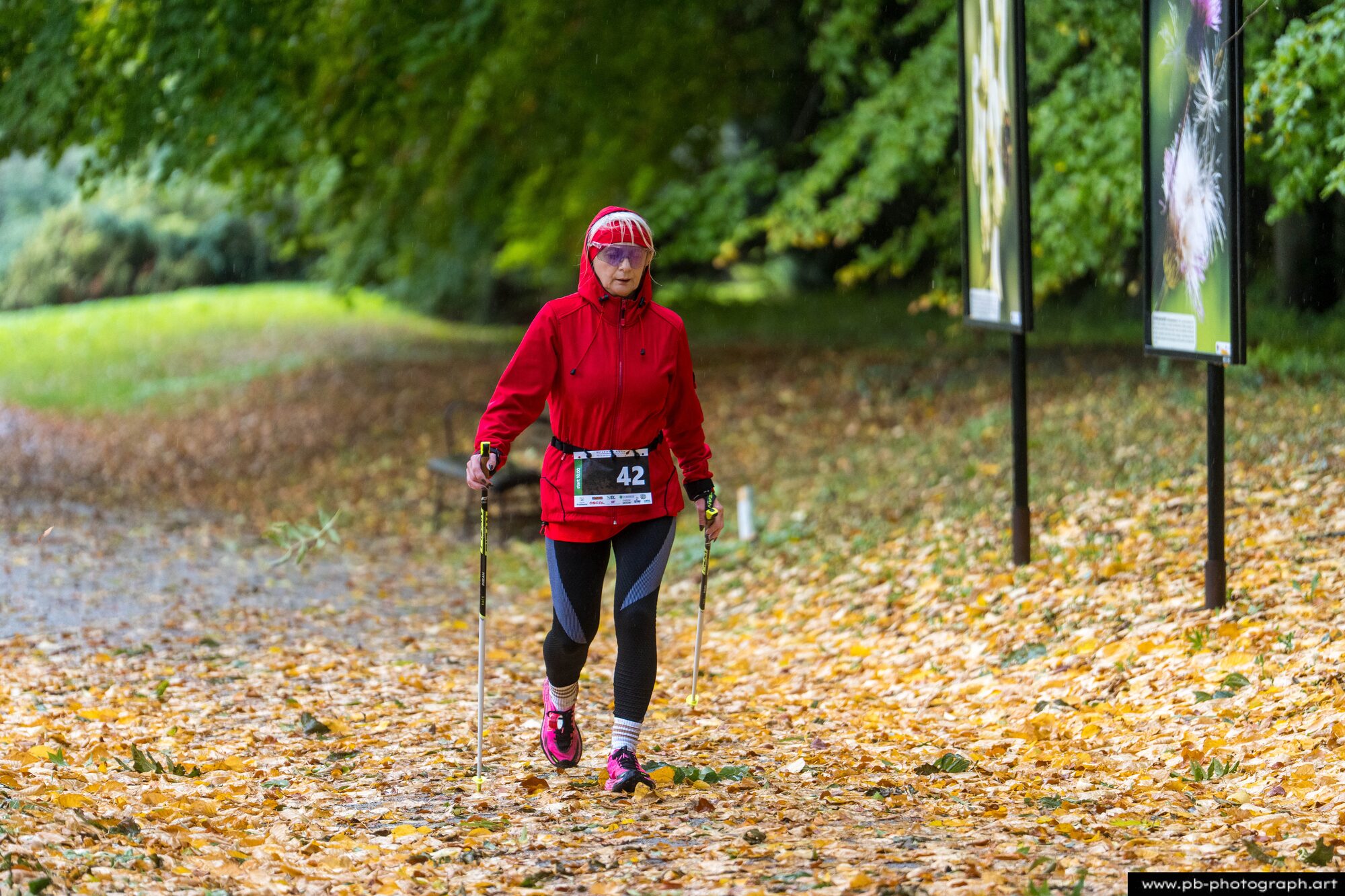 Uczestniczka z kijkami nordic walking w czerwonej kurtce na jesiennej trasie biegu
