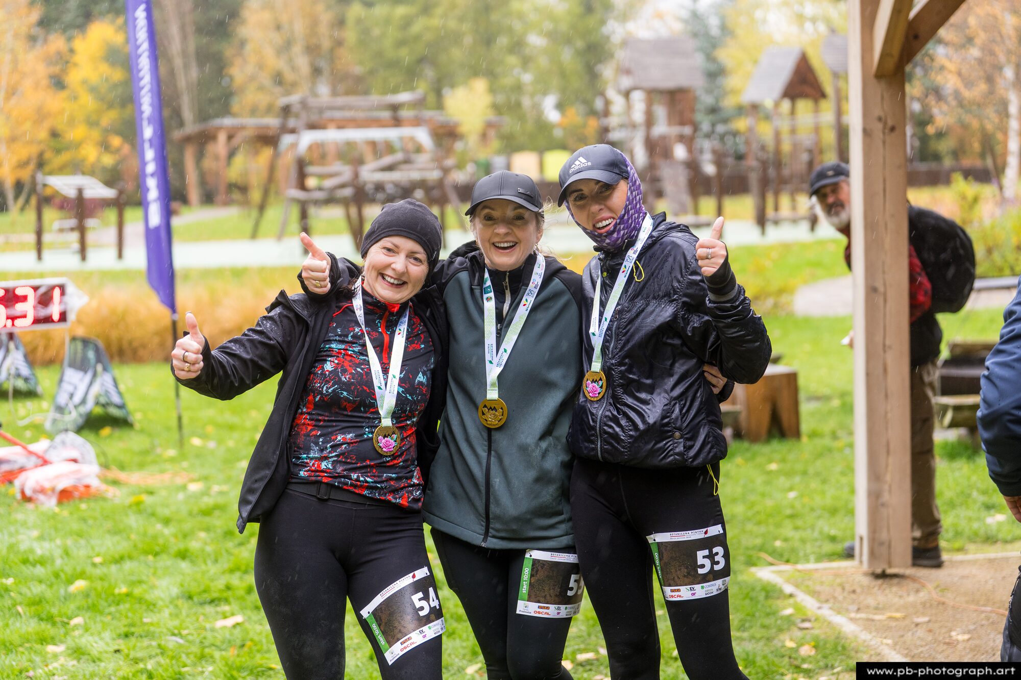 Trzy uczestniczki z medalami cieszą się po ukończeniu Botanicznej Piątki w deszczu