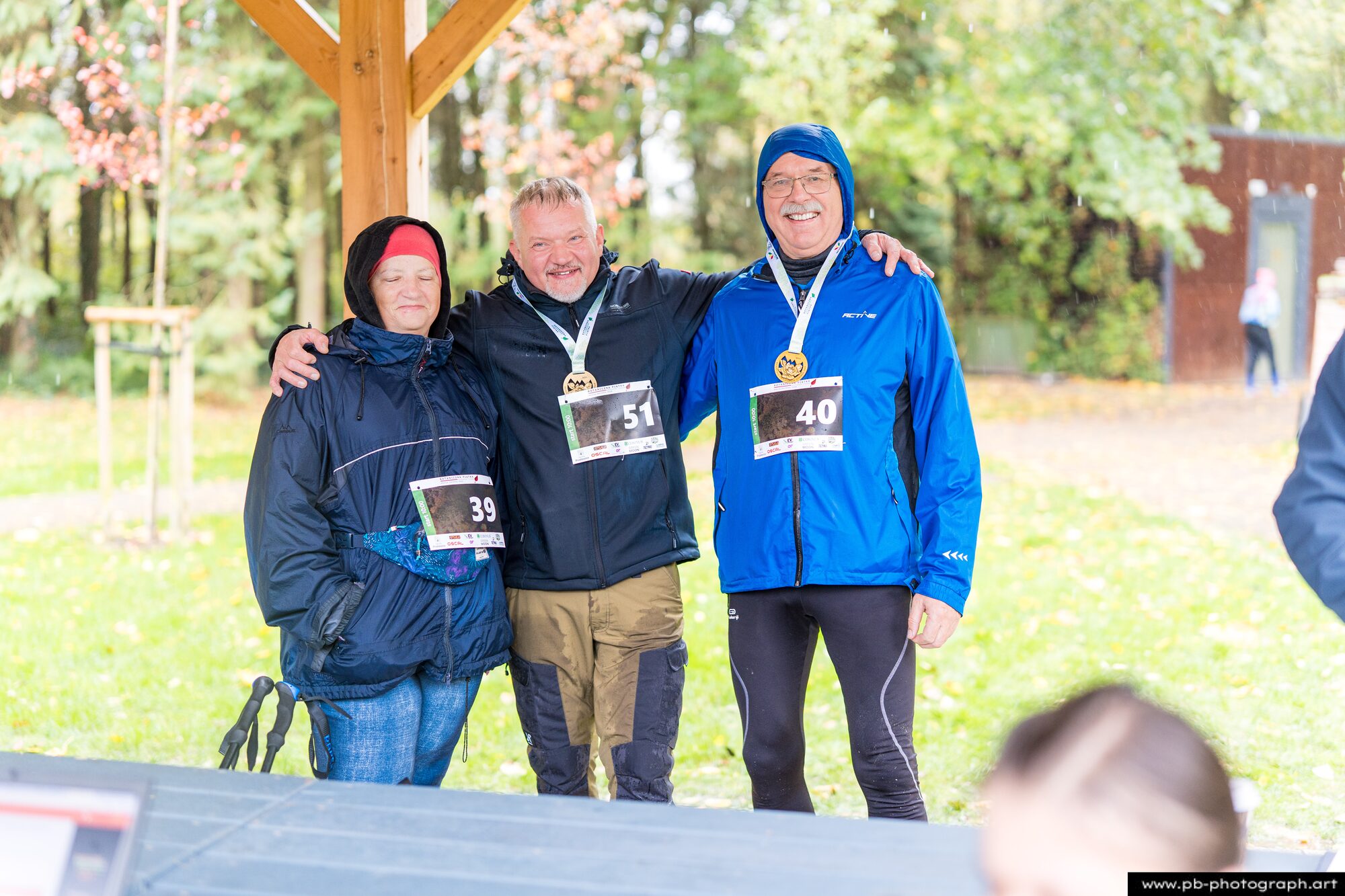 Trzech uczestników z medalami pozuje razem na tle jesiennego ogrodu